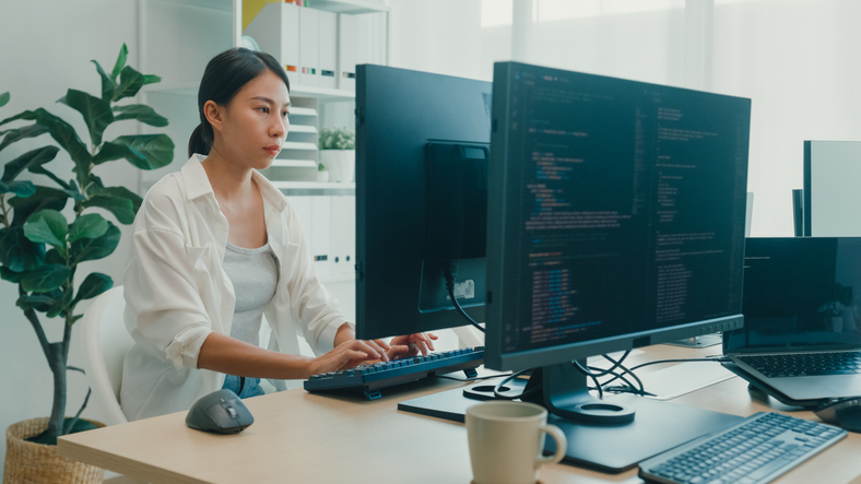 Young Asian woman software developers using computer to write code sitting at desk with multiple screens work at office. Programmer development. -