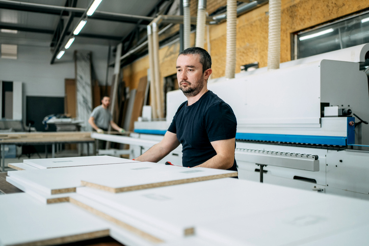 Factory technician operating a control panel with colorful buttons while coworkers review data on a tablet.