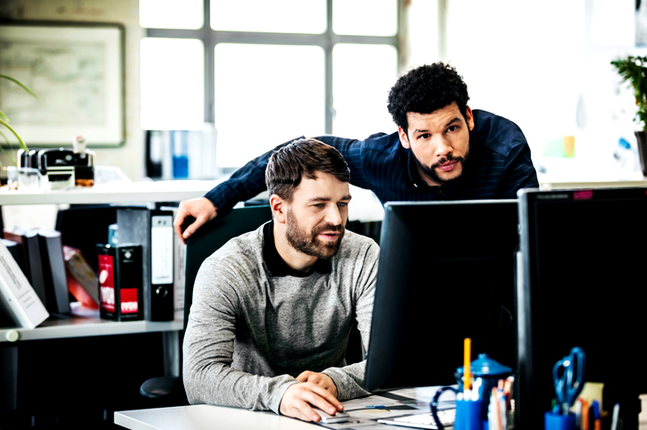 Man using a digital tablet in a dark office, illuminated by the screen and city lights reflecting through the window.