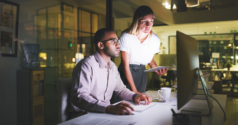 Shot of two young businesspeople working late together on a computer in their office at night